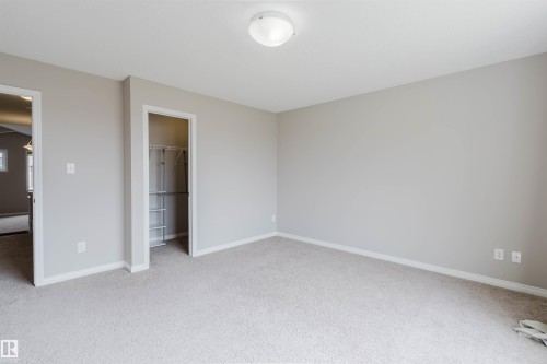 Neutral-toned room featuring light-colored carpet flooring, a flush-mount ceiling light fixture, and a built-in closet with wire shelving - 16627 18 Avenue, Edmonton, AB 