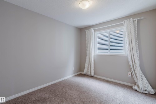 Bedroom featuring a window with white louvered blinds, neutral wall paint, and light brown carpet flooring - 16627 18 Avenue, Edmonton, AB 