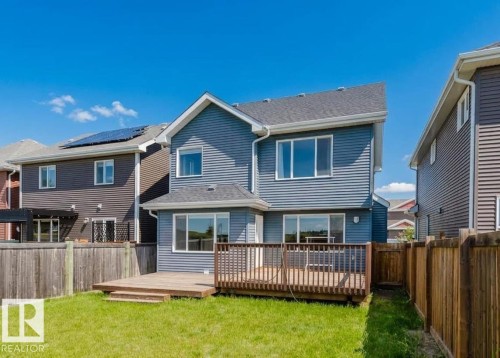 Rear exterior featuring blue horizontal siding, a multi-level wood deck, a sliding glass door, and multiple windows - 16627 18 Avenue, Edmonton, AB 