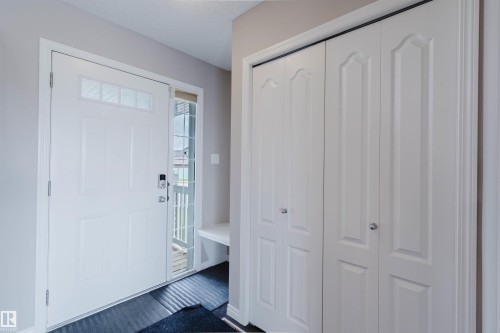 Entryway featuring a white paneled door with transom window, glass sidelight, bi-fold closet doors, and built-in bench seating - 16627 18 Avenue, Edmonton, AB 