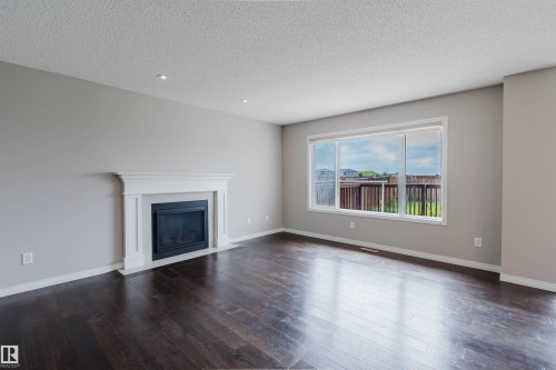 Living area featuring a traditional white mantel fireplace, dark wood-finish flooring, and a large window - 16627 18 Avenue, Edmonton, AB 