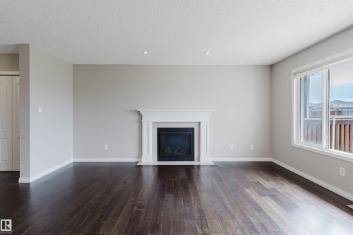 Spacious interior featuring dark wood-finish flooring, a white fireplace with a mantel, recessed lighting, and a large window - 16627 18 Avenue, Edmonton, AB 