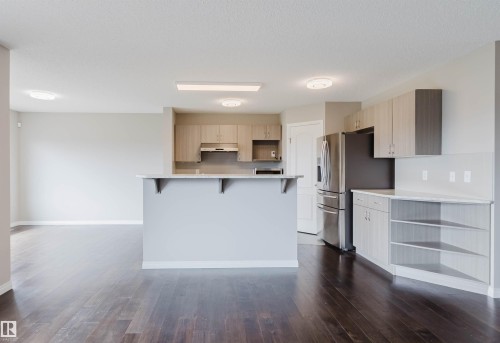 Expansive kitchen area featuring a central island with a breakfast bar, stainless steel appliances, light-toned cabinetry, and dark wood-finish flooring - 16627 18 Avenue, Edmonton, AB 