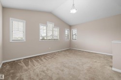 Spacious room featuring vaulted ceilings, multiple windows with blinds, a neutral color palette, and wall-to-wall carpeting - 
