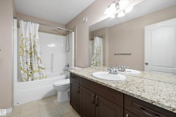 Bathroom featuring a dual-sink vanity with a light-toned countertop, a full-width mirror, and dark wood-finish cabinetry - 