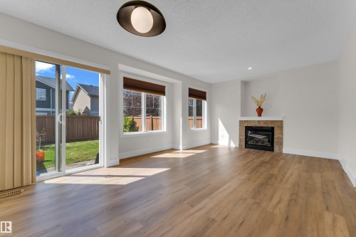 Spacious living area featuring wood-finish flooring, a contemporary fireplace with a stone surround, and multiple windows - 64 14208 36 Street, Edmonton, AB 