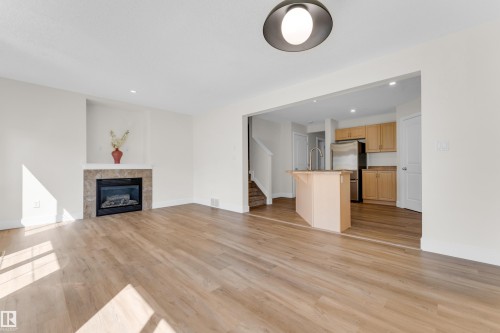 Spacious living area featuring wood-finish flooring, a tiled fireplace with a mantel, and an open concept layout - 64 14208 36 Street, Edmonton, AB 