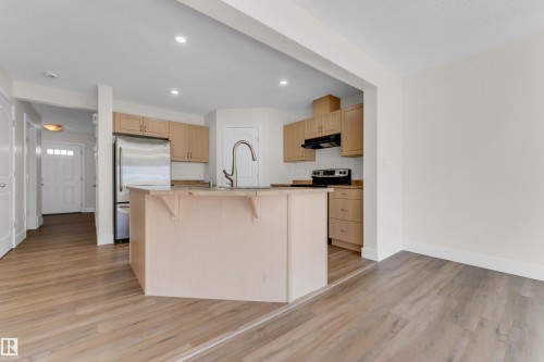 Kitchen featuring a central island with an integrated sink, light wood-finish cabinetry, stainless steel appliances, and recessed lighting - 64 14208 36 Street, Edmonton, AB 