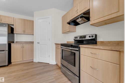 Kitchen featuring stainless steel appliances, light wood-finish cabinetry, neutral countertops, and wood-finish flooring - 64 14208 36 Street, Edmonton, AB 