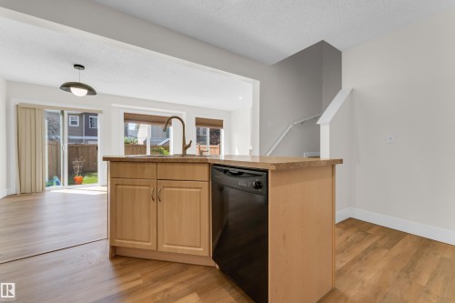 Kitchen island featuring a single-basin sink with a gooseneck faucet, light wood-finish cabinetry, and an integrated dishwasher - 64 14208 36 Street, Edmonton, AB 