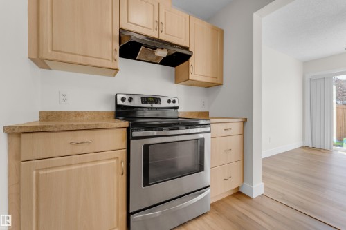 Kitchen featuring light wood cabinetry, stainless steel range with overhead ventilation, and a textured countertop - 64 14208 36 Street, Edmonton, AB 