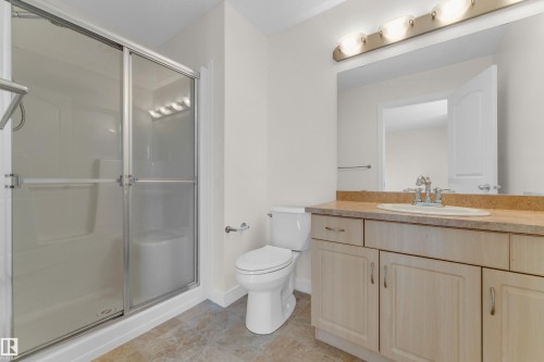 Bathroom featuring a glass-enclosed shower with integrated seating, a vanity with a light-toned countertop, a rectangular undermount sink with a chrome faucet, and a large wall-mounted mirror with overhead lighting - 64 14208 36 Street, Edmonton, AB 
