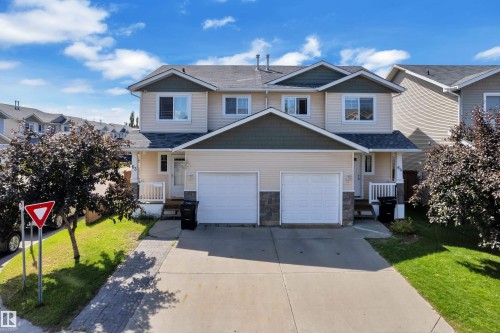 Duplex exterior with light-colored siding, dark gabled roof accents, and two single-car garages - 64 14208 36 Street, Edmonton, AB 