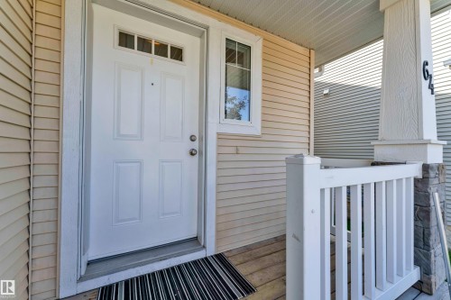 Front entryway featuring a paneled white door with transom window, light-colored horizontal siding, a wood-finish porch floor, white railing, and a stone-clad pillar - 64 14208 36 Street, Edmonton, AB 