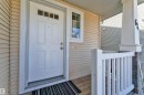 Front entryway featuring a paneled white door with transom window, light-colored horizontal siding, a wood-finish porch floor, white railing, and a stone-clad pillar - 64 14208 36 Street, Edmonton, AB 