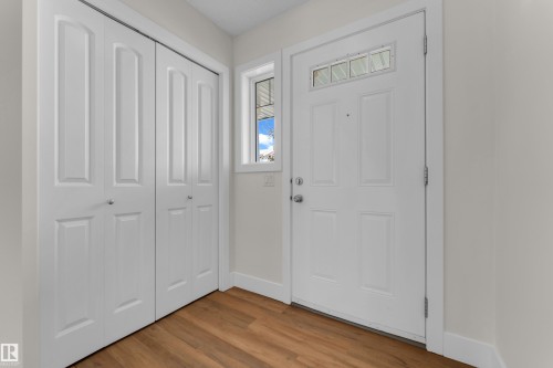 Entryway featuring wood-finish flooring, a white paneled entry door with decorative glass transom, and a side window - 64 14208 36 Street, Edmonton, AB 