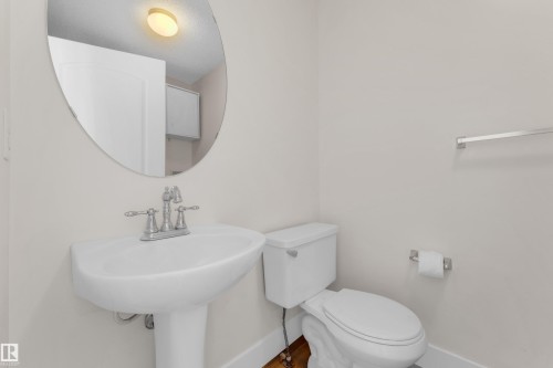 White pedestal sink with chrome faucet, oval wall mirror, and a white toilet - 64 14208 36 Street, Edmonton, AB 