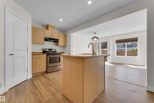 Kitchen with light wood-finish cabinetry, stainless steel appliances, and a central island with an integrated sink - 64 14208 36 Street, Edmonton, AB 