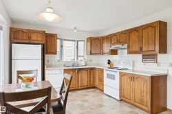 Kitchen featuring extensive wood cabinetry, white appliances, a bay window, white tiled backsplash, and light-toned flooring - 
