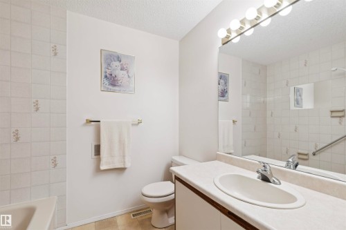 Bathroom featuring a spacious vanity with integrated sink, a large wall-mounted mirror, and tile-surround bathtub - 9315 168 Avenue Nw, Edmonton, AB 