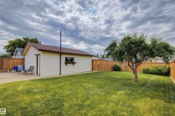 Spacious backyard featuring a detached garage with vinyl siding, a well-maintained lawn, a mature tree, and a wood privacy fence - 