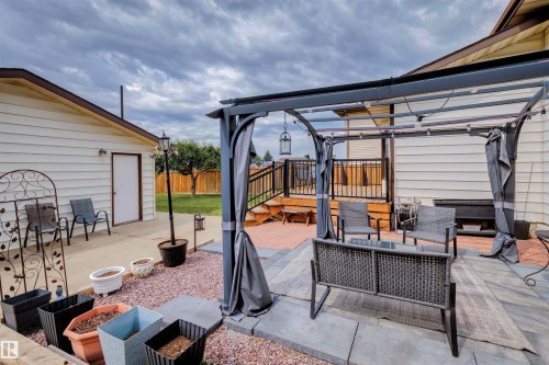 Backyard patio featuring a pergola with retractable privacy screens, a raised wooden deck with black railings, and a concrete patio area - 9315 168 Avenue Nw, Edmonton, AB 