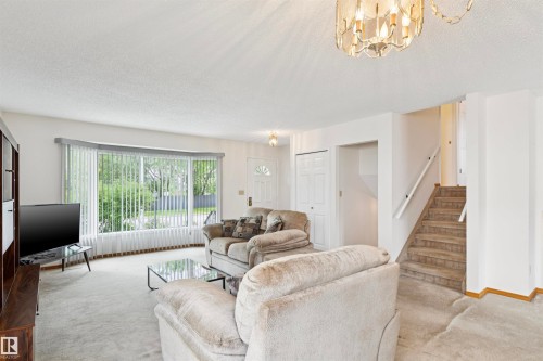 Living area featuring light-colored carpeting, a large bay window, and a chandelier-style light fixture - 9315 168 Avenue Nw, Edmonton, AB 