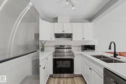 U-shaped kitchen featuring white cabinetry and countertops, stainless steel appliances, a black faucet, and wood-finish flooring - 