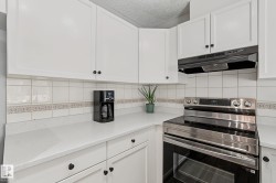 Kitchen featuring white cabinetry, solid surface countertops, white tile backsplash with decorative accent, and a stainless steel range with a built-in exhaust hood - 