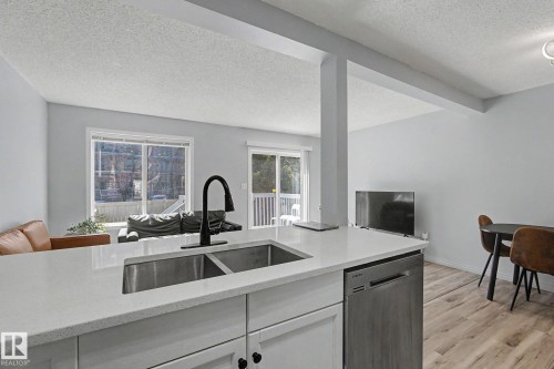 Kitchen island featuring a dual-basin stainless steel sink with a matte black faucet, light-toned countertop, and integrated stainless steel dishwasher - 5 14603 Miller Boulevard, Edmonton, AB 