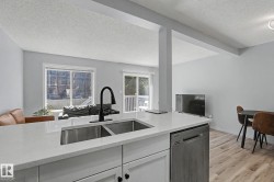 Kitchen island featuring a dual-basin stainless steel sink with a matte black faucet, light-toned countertop, and integrated stainless steel dishwasher - 