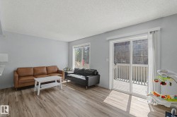 Spacious living area featuring wood-finish flooring, light gray wall paint, and a sliding glass door leading to an outdoor deck - 