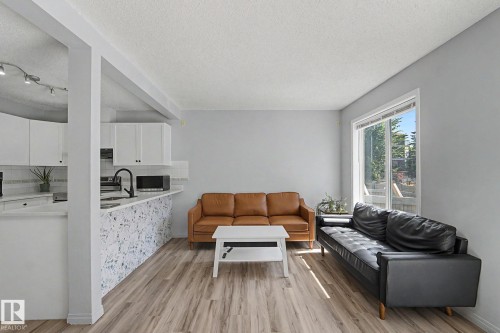 Open concept living area featuring wood-finish flooring, a large window, and light gray walls - 5 14603 Miller Boulevard, Edmonton, AB 