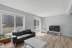 Living area featuring light gray walls, wood-finish flooring, a large window, and a sliding glass door opening to an exterior deck - 
