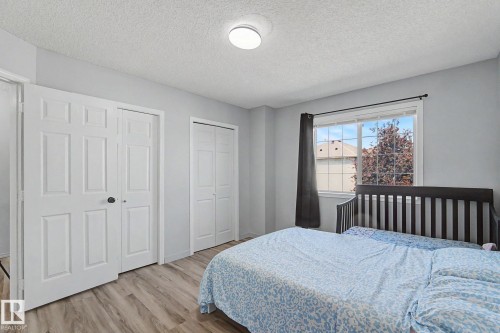 Bedroom featuring light wood-finish flooring, light gray wall paint, a window with exterior residential visibility, and two white bi-fold closet doors - 5 14603 Miller Boulevard, Edmonton, AB 