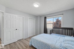 Bedroom featuring light wood-finish flooring, light gray wall paint, a window with exterior residential visibility, and two white bi-fold closet doors - 