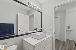 Bathroom vanity featuring a rectangular vessel sink with a matte black faucet, a large framed mirror, and a modern four-light vanity fixture - 
