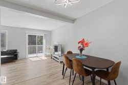 Open-concept living area featuring light wood-finish flooring, a modern flush-mount light fixture, and a sliding glass door leading to an outdoor balcony - 