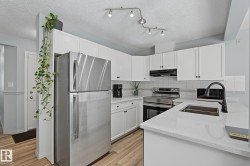 Contemporary kitchen featuring white cabinetry, light-toned countertops, stainless steel appliances, a black faucet, and wood-finish flooring - 
