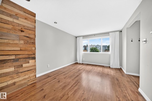 Room featuring wood-finish flooring, a prominent wood-panel accent wall, recessed ceiling lighting, and a large window with white trim - 32 Mcleod Place, Edmonton, AB 