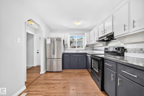 Kitchen featuring wood-finish flooring, two-tone cabinetry with white upper and dark lower cabinets, a subway tile backsplash, and a window above the sink - 32 Mcleod Place, Edmonton, AB 