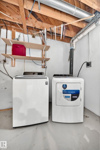 Dedicated laundry area featuring a washer and dryer, exposed wood beam ceiling, concrete flooring, and wall-mounted shelving - 32 Mcleod Place, Edmonton, AB 
