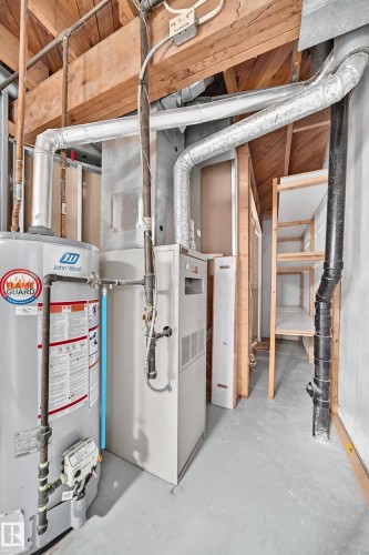 Utility area featuring a water heater, furnace, exposed wood ceiling joists, and open shelving - 32 Mcleod Place, Edmonton, AB 