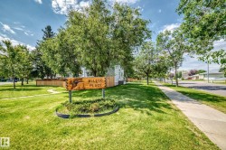 Expansive green space featuring a carved wooden sign, mature trees, and a concrete sidewalk - 