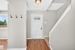 Entryway featuring wood-finish flooring, a white paneled door with decorative glass, and a staircase with carpeted treads - 
