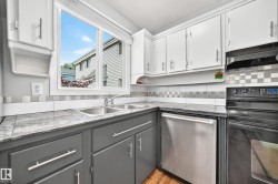 Kitchen featuring a dual-basin stainless steel sink under a window, light gray upper cabinetry, and dark gray lower cabinetry - 