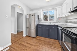Kitchen featuring wood-finish flooring, two-tone cabinetry with white upper and dark lower units, a window over the sink, and a tiled backsplash - 