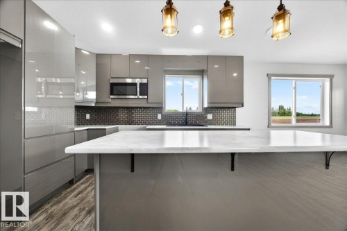 Contemporary kitchen featuring gray high-gloss cabinetry and a spacious island with a light-toned countertop - 1 Whitetail Way, Mundare, AB 