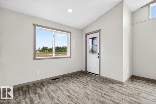 Room featuring wood-finish flooring, a white paneled door with windowpanes, and a large window with gray trim - 1 Whitetail Way, Mundare, AB 