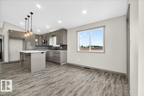 Modern kitchen featuring high-gloss cabinetry, dark tile backsplash, and a central island with white countertop - 1 Whitetail Way, Mundare, AB 